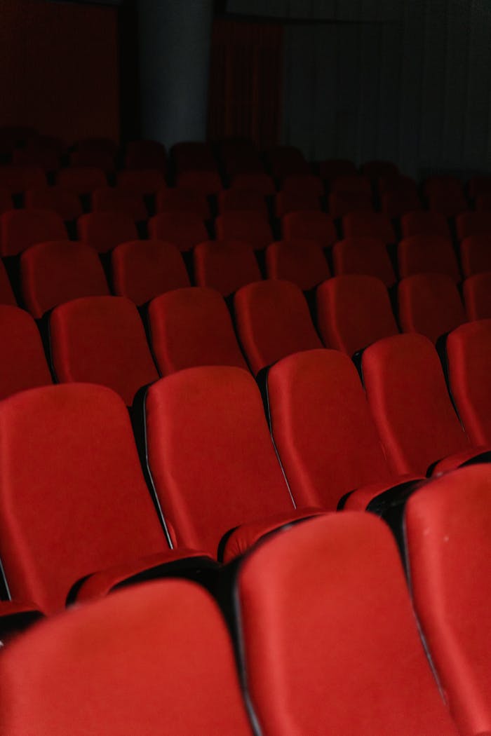 Empty cinema hall with rows of red theater seats, creating a dramatic and moody atmosphere.